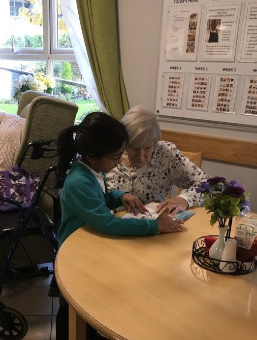 A Year 2 pupil looks at a book with a care home resident