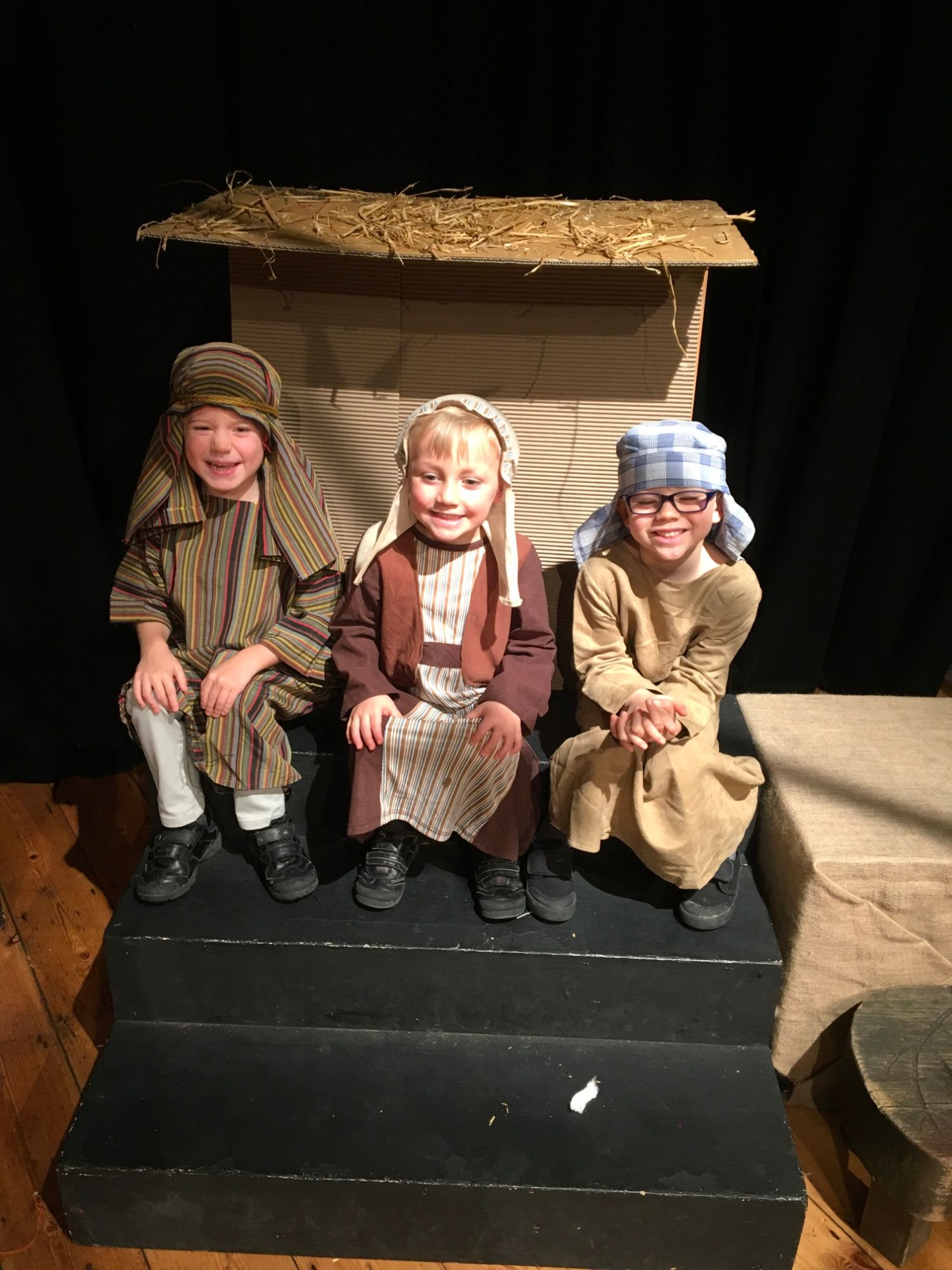 Three children sit on the stage dressed as shepherds