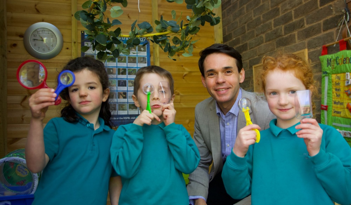 Stephen Ward smiling at the camera with a group of three Stephen Perse Cambridge Junior School students blowing bubbles.